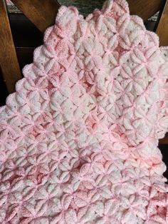 a pink and white crocheted blanket sitting on top of a wooden chair