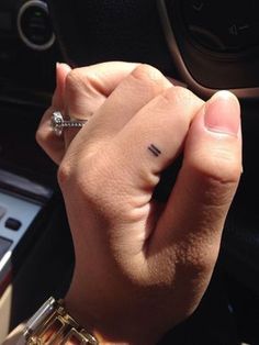 a woman's hand with a small tattoo on her left index finger, in front of a car steering wheel