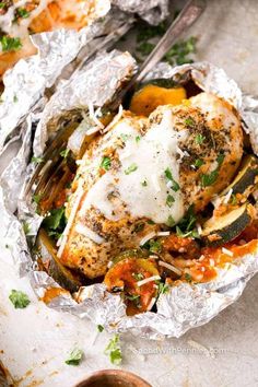 chicken wrapped in foil with vegetables and cheese on top, ready to be eaten from the oven