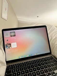 an open laptop computer sitting on top of a white bed next to a wall with pictures