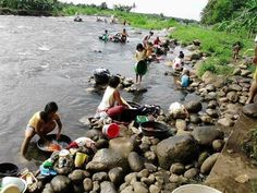 many people are washing their clothes in the river while others stand and sit on rocks