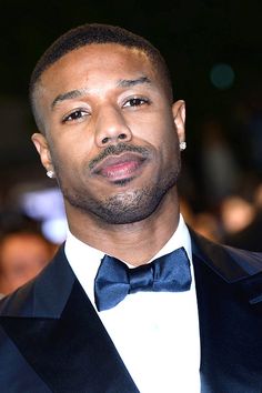 a close up of a person wearing a tuxedo and bow tie with people in the background