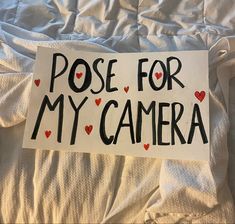 a sign that says pose for my camera on top of a white sheeted bed