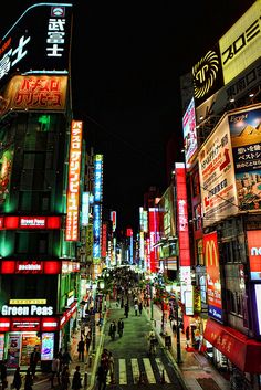 a city street filled with lots of neon signs and people walking on the side walk