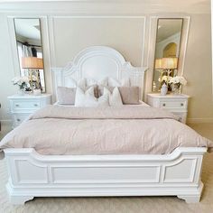 a large white bed sitting in a bedroom next to two nightstands and a mirror