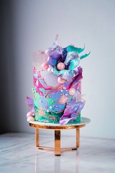 a multi - colored cake with frosting and decorations on a stand