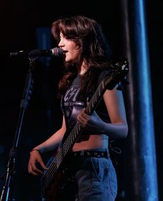 a woman holding a guitar while standing in front of a microphone