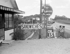 black and white photograph of an old gas station with signs on the side of the road