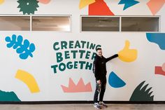 a man standing in front of a colorful wall with the words creating better together on it