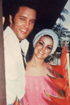 a man standing next to a woman wearing a white dress and head scarf in front of a tree