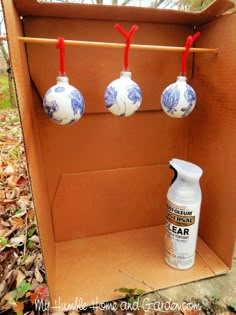 an open cardboard box with three ornaments hanging from the top and one bottle on the bottom