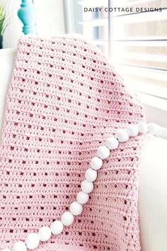 a pink crocheted blanket sitting on top of a white couch next to a window