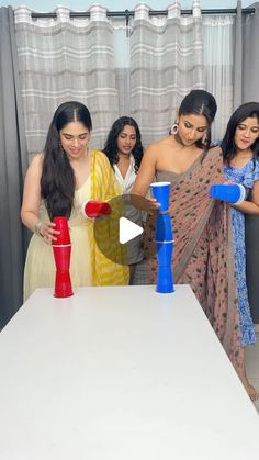 four women are standing around a table with plastic cups and vases in front of them