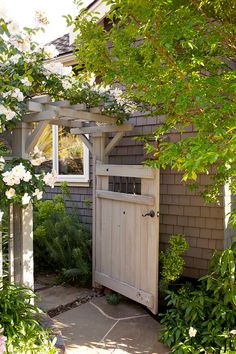 a wooden door is open in front of a house with white flowers on the bushes