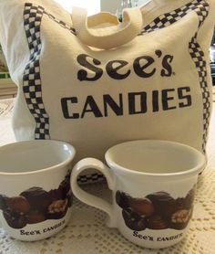 two coffee mugs sitting on top of a table next to a bag and pillow