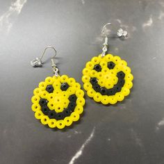 a pair of yellow and black beaded earrings with smiley face on them sitting on a table