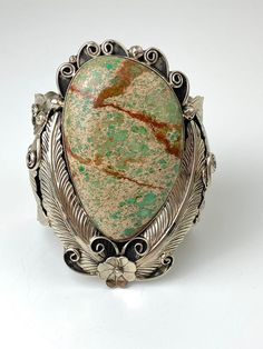 Vintage Artisan Natural Sea Sediment Jasper Cuff Bracelet- Beautifully made by Navajo artist Percy Spencer - piece is signed- Substantial heavy rigid cuff - Navajo or coin silver, non-magnetic- Huge stone surrounded by very intricate silver work with feathers, flowers, swirls and stamp work on the arm cuff- The jasper stone is natural with lots of green, dark brown matrix and a tan colored background.  Almost perfect teardrop shape.- Face of cuff measures 3.5" x 2.5"- Width of arm band 2"- Jaspe Bohemian Engraved Cuff Bracelet Collectible, Bohemian Patina Cuff Bracelet Collectible, Bohemian Style Collectible Cuff Bracelet With Patina, Handmade Bohemian Cuff Bracelet Collectible, Bohemian Handmade Collectible Cuff Bracelet, Percy Spencer, Sea Jasper, Shape Face, Quartz Rock