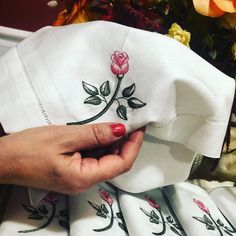 a hand is stitching on the side of a white cloth with pink flowers and leaves