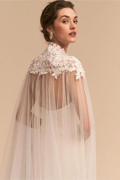 a woman wearing a wedding veil with flowers on the top and sleeves, standing in front of a beige background