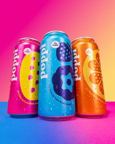 three soda cans with water droplets on them in front of a multicolored background