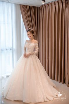 a woman standing in front of a window wearing a wedding dress with long sleeves and sequins