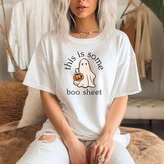 a woman with grey hair sitting on a bed wearing a white shirt that says, this is some boo sheet