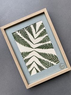 an art work with leaves in a wooden frame on a gray surface, showing the pattern