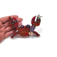 a hand holding a small red and black animal brooch with two eyes on it's back