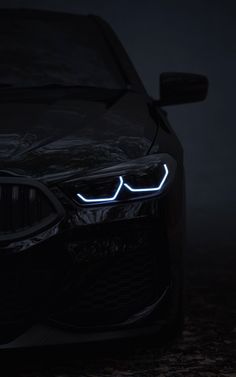 the front end of a black car with its lights on in the dark, it is glowing