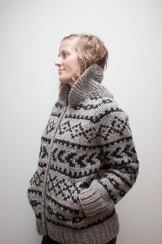 a woman wearing a gray and black knitted sweater standing in front of a white wall