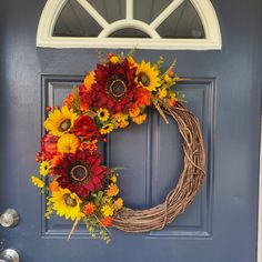 a wreath with sunflowers and other flowers is hanging on the front door's blue door