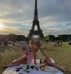 two women sitting on a blanket in front of the eiffel tower reading a newspaper