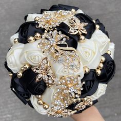 the bridal bouquet is adorned with black and white roses, brooches, and pearls