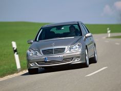 a silver car driving down a road next to a green grass covered field on a sunny day