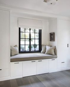 a window seat in the corner of a room with white cupboards and pillows on it