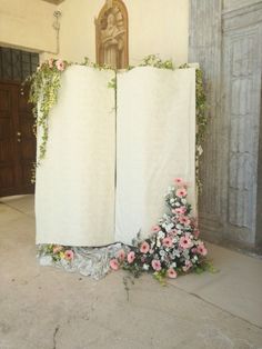 two white curtains with flowers on them in front of a statue and wooden door behind them