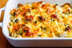 a casserole dish with cheese and broccoli in it on a wooden table