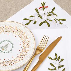 a table setting with gold utensils and embroidered napkins