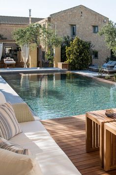 an outdoor swimming pool surrounded by wooden decking and lounge chairs with pillows on it