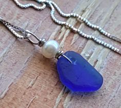 a blue sea glass and pearl necklace on a wooden surface with a chain attached to it