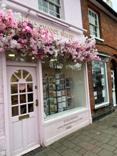 a store front with pink flowers hanging from it's windows