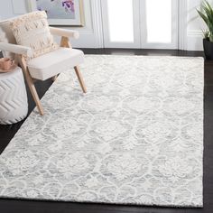 a white rug with an ornate design on the floor in front of a chair and potted plant