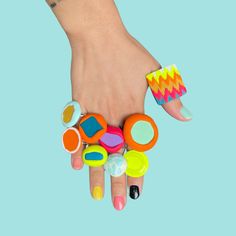 a woman's hand with colorful nail polishes and rings on her fingers, against a blue background