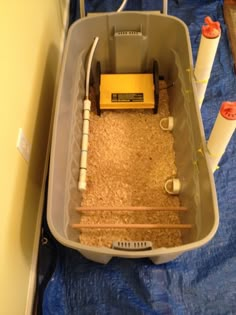 a plastic container filled with sand and water next to pipe holders on top of a blue tarp