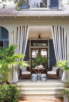 the front porch is decorated with blue and white striped curtains, wicker chairs, and potted palm trees