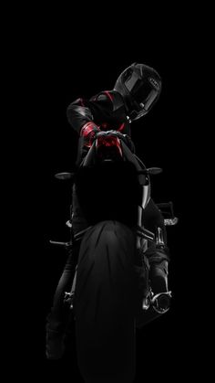 a man riding on the back of a motorcycle in black and red colors at night