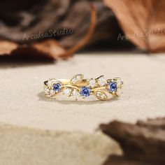 a gold ring with blue and white stones sits on top of a leafy surface