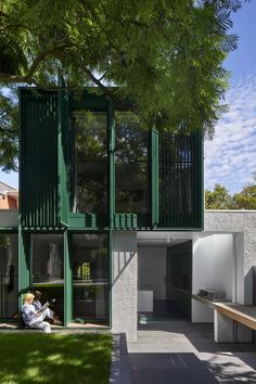 a person sitting on the ground in front of a building with green doors and windows