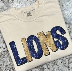 Gold & navy faux sequin Lions shirts.   Comfort Colors brand unisex short sleeve shirts. Sizes adult small-2xl are available. Ivory, white, or gray available in adult sizes.  Comfort Colors brand youth shirts in sizes xs-xl. Youth are only available in short sleeve tees. White and gray are the colors available in youth. Please choose the shirt size from the drop down box.   In the case that my distributors are out of stock on a certain size/color, I will message you on Etsy to arrange a refund or change in order. Please download the Etsy app so you can receive messages. In the case that you do not respond, the order will be canceled because I do not have access to your contact info. Thank you for understanding. Each item ordered from my shop is custom made. No two items will be identical. Spirit Wear Shirts, Back To School Shirts, Team Spirit Shirts, School Spirit Wear, Color Outfits, School Spirit Shirts, Lion Shirt, Gold Outfit, Spirit Shirts