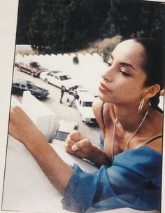 a woman sitting on top of a white car next to a parking lot filled with parked cars